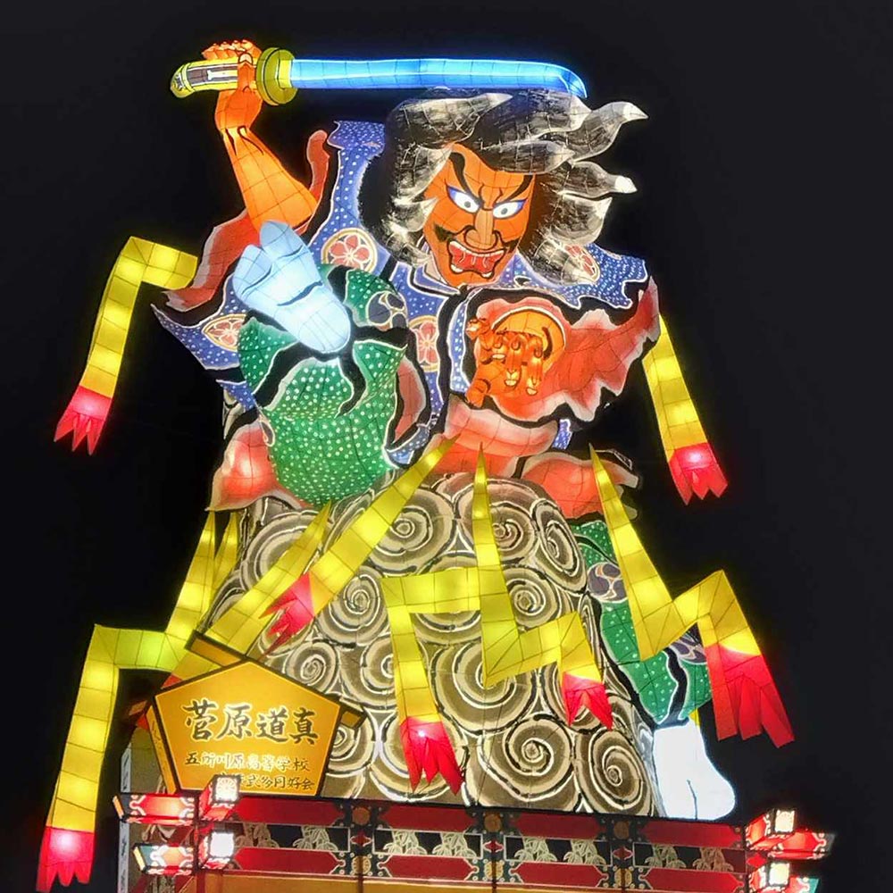 A brightly-coloured Nebuta Festival float. A warrior with a sword drawn sits atop the float.
